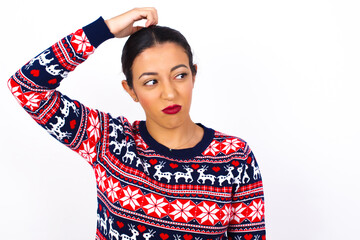 Young beautiful Arab woman wearing Christmas sweater against white wall saying: Oops, what did I do? Holding hand on head with frightened and regret expression.