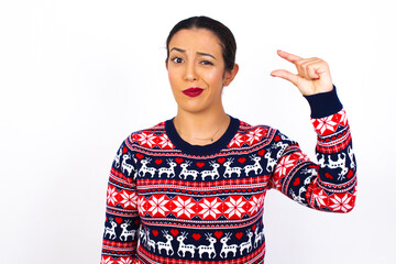 Upset Young beautiful Arab woman wearing Christmas sweater against white wall, shapes little...