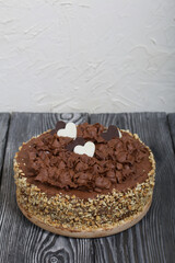 Chocolate cake with cream and peanuts. Decorated with chocolate hearts. On pine boards.