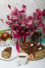 Chocolate cake with cream and peanuts. Decorated with chocolate hearts. Nearby is a cup of coffee and a bouquet of chrysanthemums.