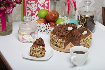 Chocolate cake with cream and peanuts. Decorated with chocolate hearts. Nearby is a cup of coffee.