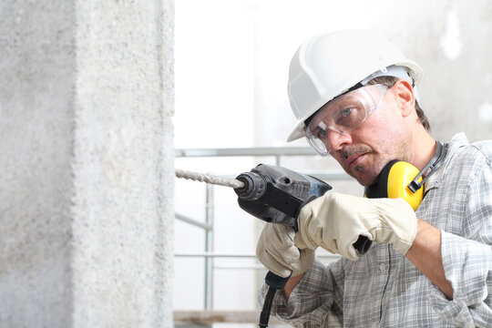 man using an electric pneumatic drill making a hole in wall, professional construction worker with safety hard hat, hearing protection headphones, gloves and protective glasses.