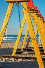 The area of the campsite. A row of swings suspended from a wooden crossbar on a sandy sea beach.