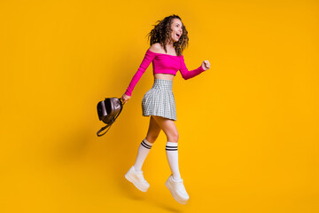 Fototapeta na wymiar Full length profile photo of lady curly hairdo open mouth bag jump wear pink cropped top unclothed shoulders mini skirt white sneakers isolated yellow color background