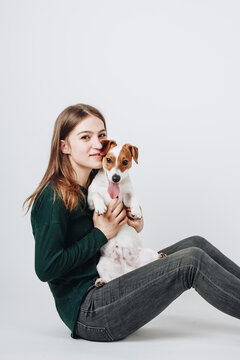 Young white woman hugs her jack russell terrier puppy. Isolated on white background. Studio portrait. Owner and her dog posing together.