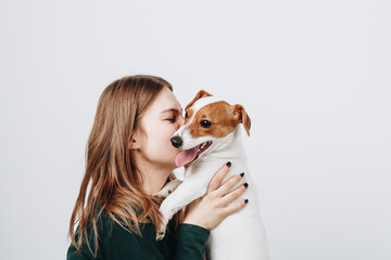Fototapeta na wymiar Cute young woman kisses and hugs her puppy jack russell terrier dog. Love between owner and dog. Isolated on white background. Studio portrait.