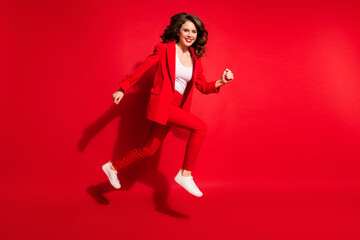 Fototapeta na wymiar Full length profile photo of pretty young lady run move toothy smiling wear jacket trousers sneakers isolated red color background