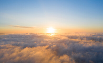 Fototapeta premium Aerial view gold sunrise over clouds in blue sky. Aerial top view cloudscape. Texture of clouds. View from above. Orange sunrise or sunset over clouds. Panorama clouds texture