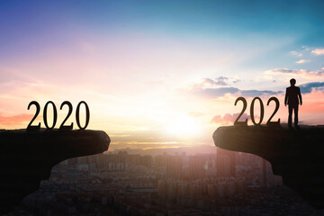 2021 concept: Silhouette of year 2021 and businessman  on mountain  with city sunset  background
