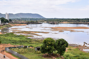 View of the Oubangui River in Bangui, Central African Republic, during the dry season, with boats, fishermen, workers collecting sand, and buildings on the river bank - obrazy, fototapety, plakaty