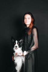 Young white woman hugs her border collie puppy. Isolated on black background. Studio portrait. Owner and her dog posing together.