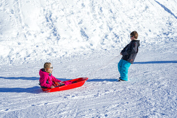 Brother pulling his sister kids toboggan sled snow. Little girl and boy enjoying sleigh ride. Child sledding. Children play outdoors in snow.