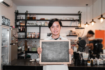 Fototapeta na wymiar asian barista standing and holding a chalkboard when work breaks