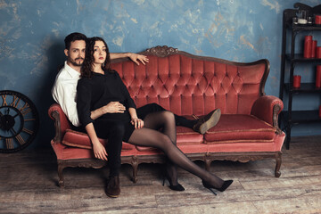 Obraz premium A young couple lies on an ancient sofa in a classic style in an interesting unusual pose. Glamorous male and female gently touch each other, old antique background copy space appartment room.