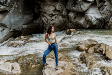 Girl is travelling in Karpathian mountains and feeling freedom. Waterfall in mountain river. Cascade waterfall and beautiful young woman