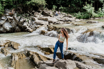 Girl is travelling in Karpathian mountains and feeling freedom. Waterfall in mountain river. Cascade waterfall and beautiful young woman