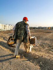 Old man wearing an army uniform taking his trash to the main big garbage bin in the neighbourhood