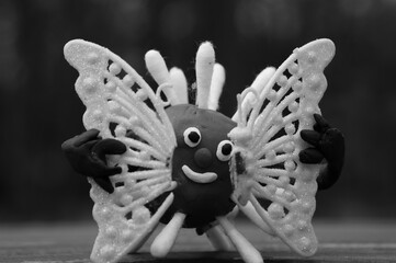 A plasticine virus figurine holds a broken butterfly in its hands.