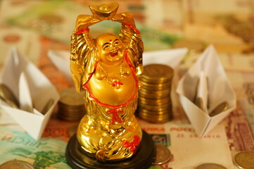 Golden Buddha statue close-up. Paper boats with coins in the background.