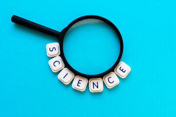 Science word made with board game letters, surrounding a magnifying glass, over a bright blue background