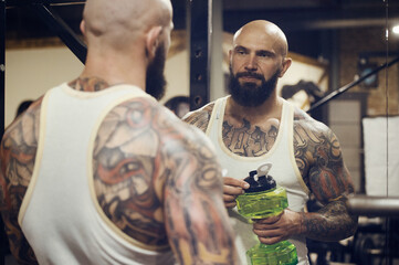 brutal tattooed man in the gym drinking water