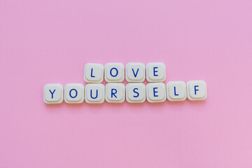 Love yourself message made with board game letters, over a soft pink background