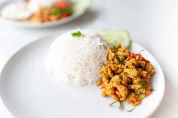 Select focus rice topped stir-fried chicken and basil on a round ceramic plate. On white marble Thai food menu for advertising media in restaurants, Branner close-up