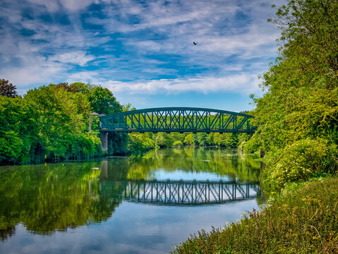 A Beautiful Summers Day In Washington, UK With A View Of The Fatfield Bridge, Reflecting In The River Wear With A Crow Flying Overhead.