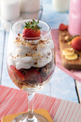 Nutritious breakfast in a glass cup with strawberries, chantilly cream, bananas, granola.