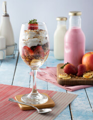 Nutritious breakfast in a glass cup with strawberries, bananas, chantilly cream, granola, almond milk.