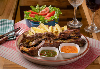 Grilled beef ribs with skin-on fries, chili sauce and chimichurri sauce, lettuce and tomato salad and a crystal glass of Jamaican water.