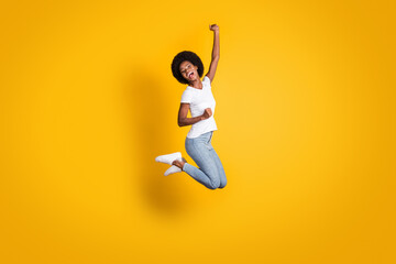 Fototapeta na wymiar Full length body size photo of cheerful happy girl with black skin jumping high keeping hand up laughing isolated on bright yellow color background