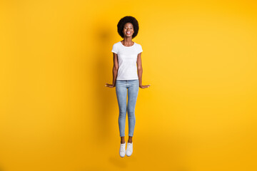 Fototapeta na wymiar Full length body size photo of funny happy girl with black skin jumping high laughing isolated on bright yellow color background