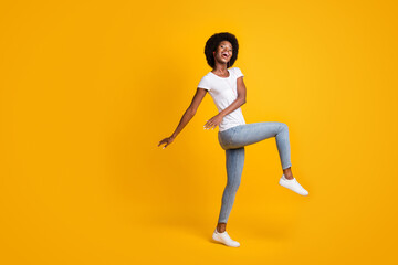Fototapeta na wymiar Full length body size photo of positive young woman with black skin listening song dancing with orange earphones isolated on bright yellow color background with empty space