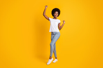 Full length body size photo of young girl with black skin listening music with headphones wearing casual outfit smiling isolated on bright yellow color background
