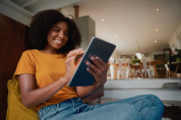 Cheerful african woman sitting at home on floor with digital tablet at home relaxing