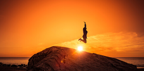 Frau hüpft von einem Felsen bei Sonnenuntergang am Strand