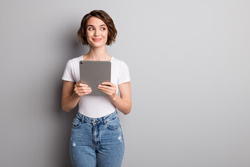 Photo of cheerful young lady hold modern device tablet look empty space isolated over grey color...