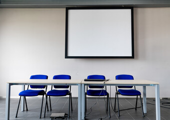 Simple presentation room front view of table and speaker's chairs with big white screen copy space behind on the wall