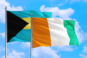 Cote D'Ivoire and Bahamas national flag waving in the windy deep blue sky. Diplomacy and...
