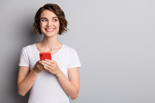 Photo of young beautiful girl happy toothy smile hold cellphone mobile look empty space isolated over grey color background