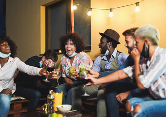 Happy multiracial friends enjoy cocktails at home on patio while wearing protective face mask under chin - Coronavirus lifestyle and prevention