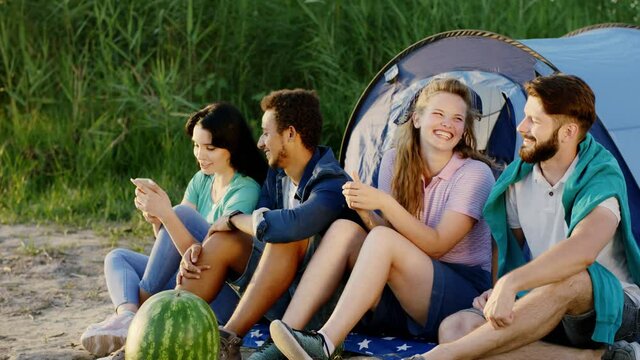 Diverse group of friends have picnic time at sunset they take some selfie pictures beside of their tent while sitting down on the grass. Shot on ARRI Alexa