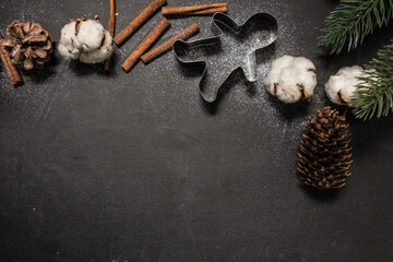 Christmas holidays spirit concept: gingerbread man or season biscuit form, cotton flowers, pine twigs, cones, cinnamon sticks and fresh snow powder on black. Creative flat lay. Top view, copy space.