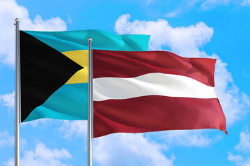 Latvia and Bahamas national flag waving in the windy deep blue sky. Diplomacy and international relations concept.