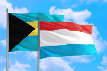 Luxembourg and Bahamas national flag waving in the windy deep blue sky. Diplomacy and international relations concept.