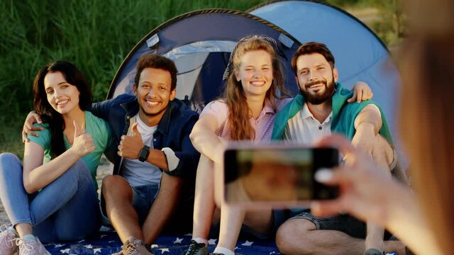 Good looking group of friends multiracial posing at the picnic beside of their tent some other friend take pictures with the phone. Shot on ARRI Alexa