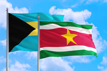 Suriname and Bahamas national flag waving in the windy deep blue sky. Diplomacy and international relations concept.