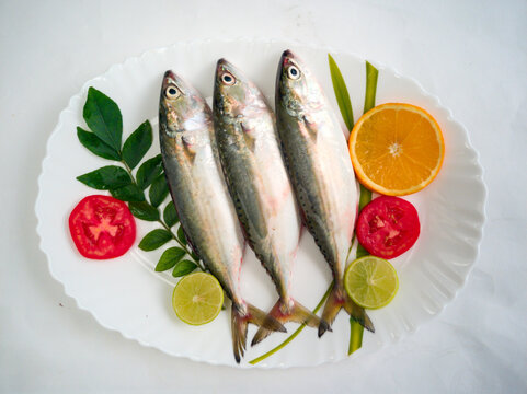 Fresh Indian Mackerel Fish Decorated with herbs and Vegetables on a white plate.