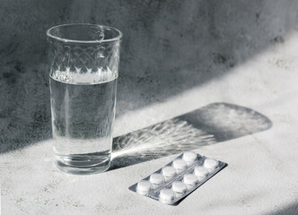 Clear glass of water and pack of pills in contrast day light on grey background. Headache or...